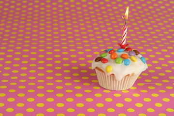 Birthday muffin with icing, sprinkles and candle