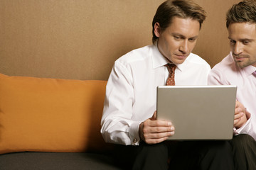 Two businessmen using laptop, sitting on sofa