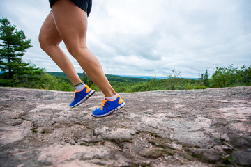 Legs of young woman wearing fitness clothing running across rocks with forest background