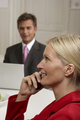 Young blond woman is phoning in front of a man who is working with a laptop, selective focus