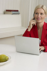 Blond woman sitting behind a laptop while phoning