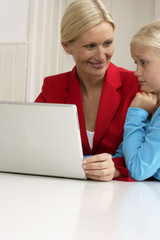 Blond girl is sitting next to her mother behind a laptop, close-up