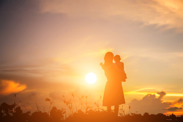 a silhouette of a happy young girl child the arms of his loving mother for a hug, in front of the sunset in the sky on a summer day.