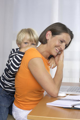 Mother phoning with a mobile phone while son (4-5 Years) embracing her form behind