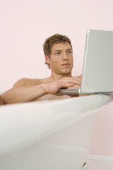 Man sitting in a bathtub, using a laptop