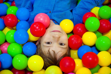 Fototapeta na wymiar Happy little kid boy playing at colorful plastic balls playground high view. Funny child having fun indoors.