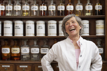 Laughing pharmacist standing in front of a shelf with glass bottles and tins