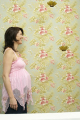 Pregnant woman standing in front of flowered wall, profile