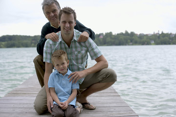 Boy, father and grandfather sitting on a wooden footbridge at a lake