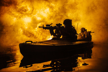 Backlit silhouette of special forces marine operators in military kayak on fire explosion...