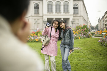 Naklejka premium Man taking a picture of two Asian women who are standing on a meadow in front of buildings, selective focus