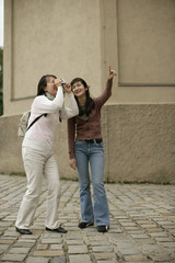Young Asian woman pointing at something while another woman is taking a picture of the shown place