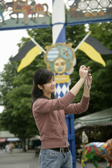 Young Asian woman standing in front of a maypole and is taking pictures with a camera, selective focus