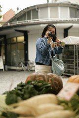 Young Asian woman taking a picture of pumpkins in a sales booth, selective focus