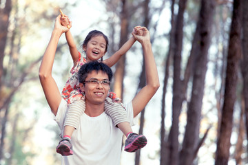 Father and daughter having fun and playing in the park and child sits on the shoulders of her father in vintage color tone