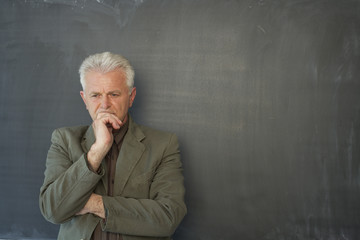 Reflective professor leaning against a blackboard