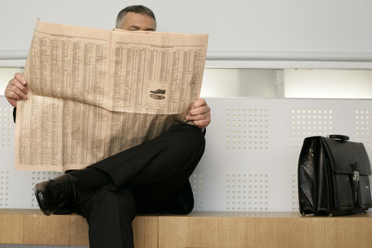 Businessman sitting on a bench reading a newspaper