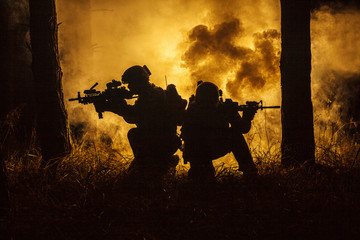 Backlit silhouette of special forces marine operators in forest on fire explosion background....