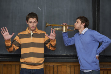 Man playing trumpet next to another man, both in front of a blackboard