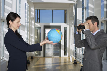 Businessman looking through field glasses to businesswoman holding a globe
