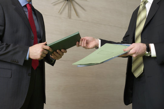 Two businessman standing in an office, handing over documents 