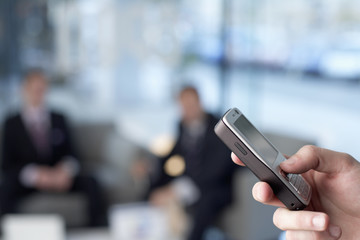Businessman holding a cell phone, two businessmen in the background