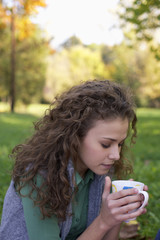 Teenage girl with curly hair holding a cup of tea in her hands, close-up