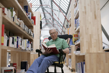 Senior man in a rocking chair reading a book, fully_released