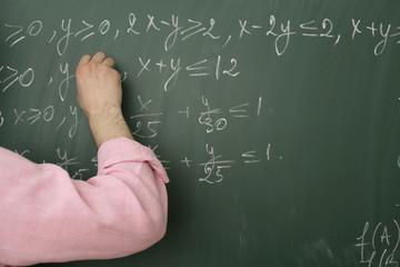 Teacher writing an arithmetic problem on blackboard