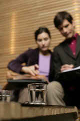 Two businesspeople poring over documents, a glass of water standing in foreground