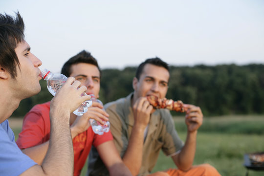Three young men eating and drinking
