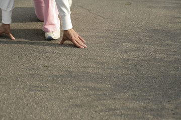 Mature woman in starter block position, focus on hands and feet