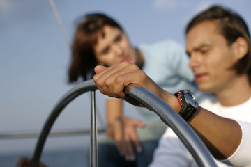 Man at steering wheel of a sailboat, woman standing behind him