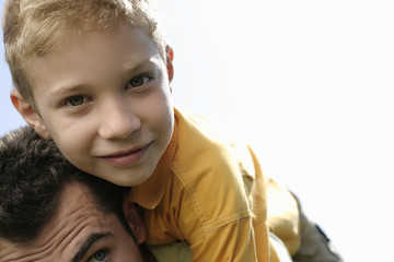 Father giving son a piggyback ride, boy looking at camera