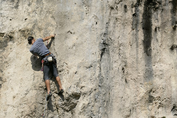 Young man with black hair climbing up a rocky wall, selective focus
