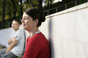 Young girl listening music about earphones, boy in background