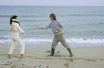 Young Couple fighting with little Sticks - Imitation of a Swordplay - Fun - Leisure Time - Beach