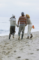 Two young Women with a Man between them strolling along the Beach - Friendship - Trip - Season