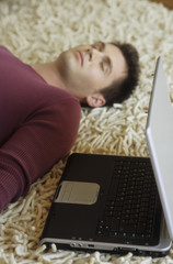 Young Man lying on a Carpet next to a Laptop sleeping - Tiredness - Relaxation - Technology - Home...