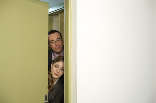 Businessman And Businesswoman Sneaking Out Of Bathroom