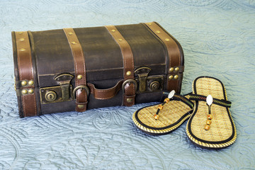 Vintage leather suitacse closed on bed, packed for travel, beaded sandals beside