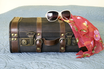 Leather vintage suitcase with tropical scarf and sunglasses draped on top, travel concept