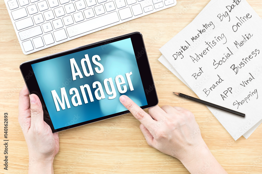 Poster Hand using tablet with Ads manager word on screen with list of digital marketing features on paper on work table,Online business concept