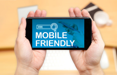 Watching two hand holding mobile phone with Mobile friendly word on screen and blur desk office...