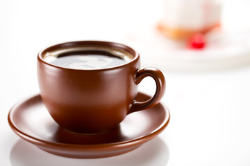 A brown cup of coffee with a cake in the background