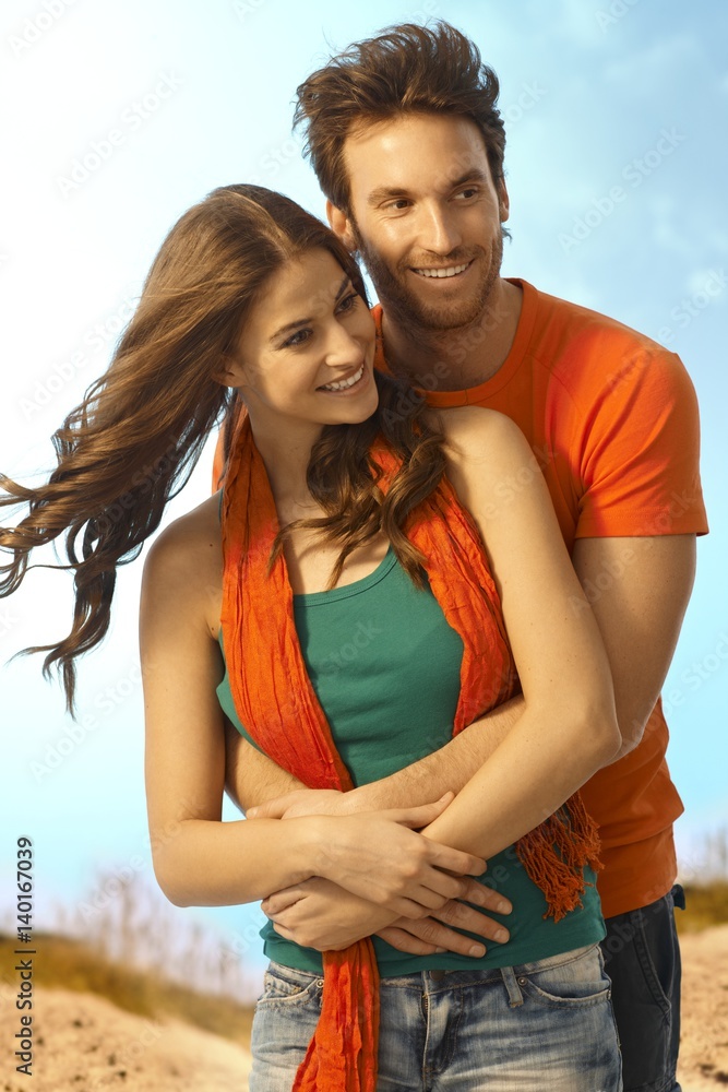 Poster happy young casual couple embracing outdoors