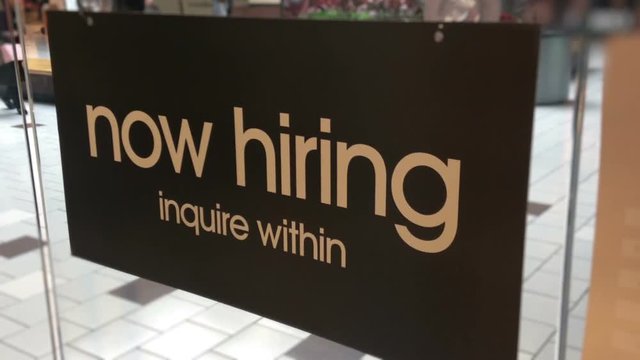 Now hiring sign on glass wall posted in shopping mall