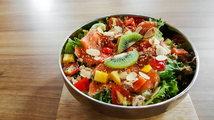 Bowl smoked salmon fruit salad on natural wood table.