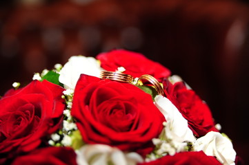 Wedding rings and wedding bouquet of red roses on wooden table, horizontally Selective focus, the background is blurred
