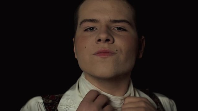portrait of a gay man who looks in the camera over black background and begins to strangle himself. Close-up over black background